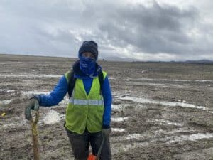 Save The Bay employee with shovel at muddy wetland restoration site