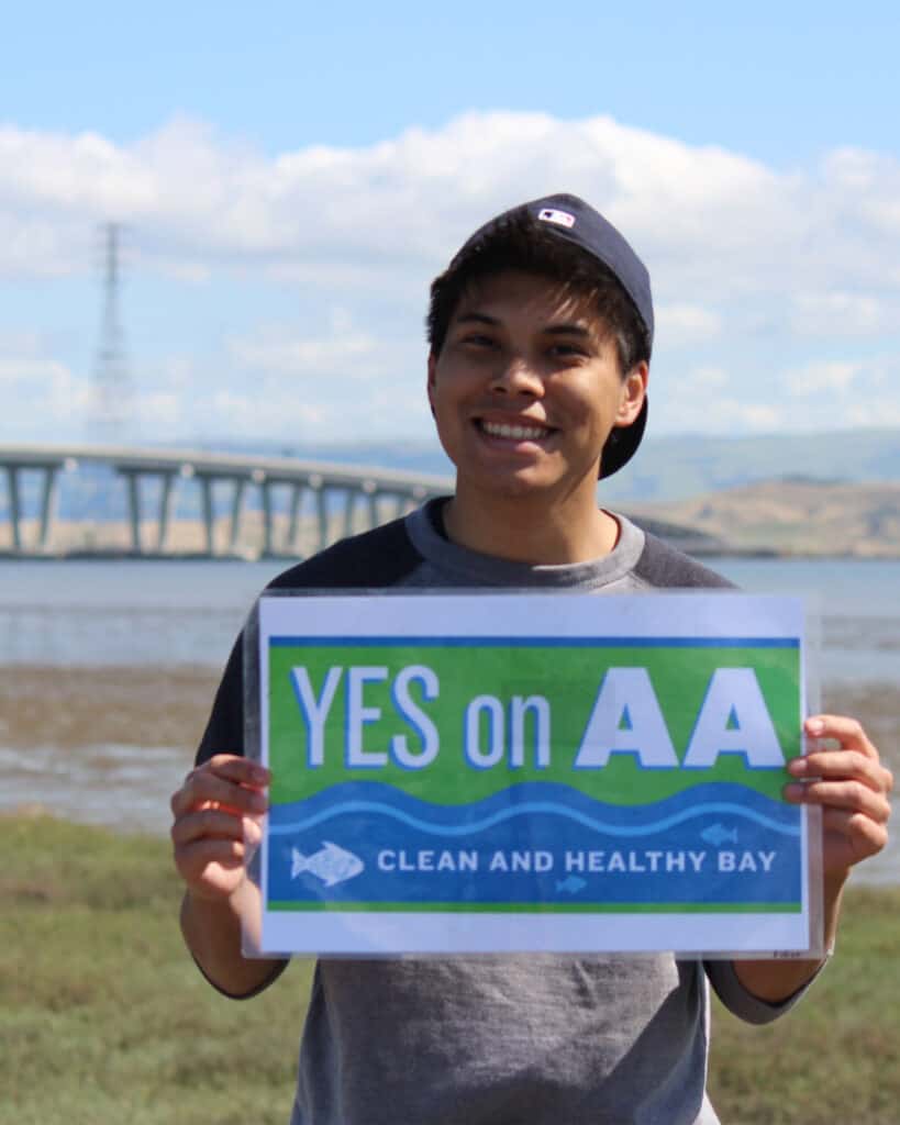 Person holding "Yes on AA" sign outside on the shoreline