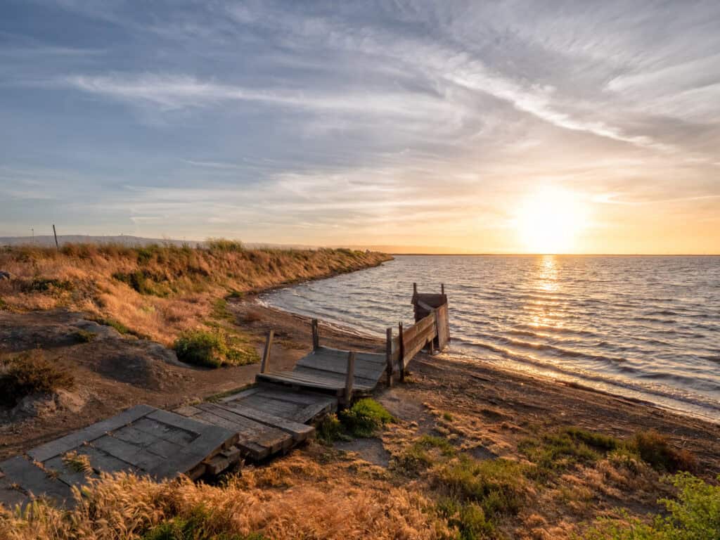 sun setting against the Alviso shoreline, with a walking path in front of it